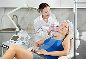 Professional female cosmetologist doing hydrafacial procedure in cosmetology clinic. Doctor use hydrogen and oxygen