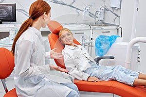 Professional female dentist communicating with pretty child patient while checking teeth