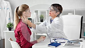 Professional female doctor checking patient neck examining glands at modern clinic white interior