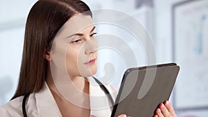 Professional female doctor with stethoscope in hospital room using tablet. Woman physician at work