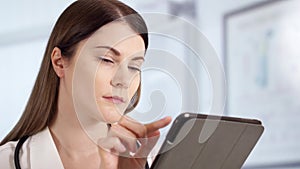 Professional female doctor with stethoscope in hospital room using tablet. Woman physician at work