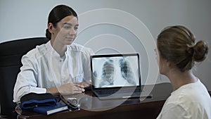 Professional female doctor tells something to female patient and showing on screen of laptop with lung x-ray image