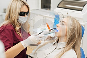 Professional female doctor uses ultraviolet lamp after making a filling on a tooth for joyful happy caucasian woman in