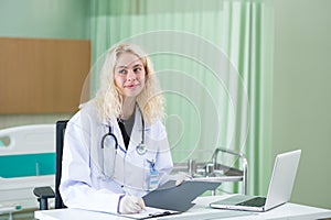 A professional female doctor in white medical coat is working on her table in the patient room. Health care Concept