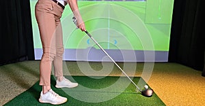 Professional female golfer playing golf indoors on golf simulator closeup