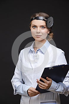 Professional Female GP Doctor Posing in Doctor`s Smock an Examination Mirror Against Black photo