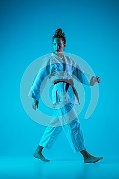 Professional female judoist posing isolated on blue studio background in neon light. Healthy lifestyle, sport concept.