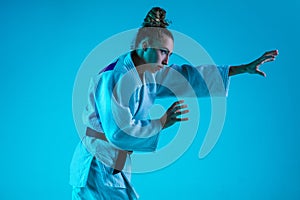 Professional female judoist training isolated on blue studio background in neon light. Healthy lifestyle, sport concept.