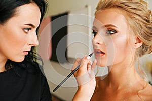 Professional female makeup artist applying cosmetics on model face use brush working at beauty salon. Woman visagist make up