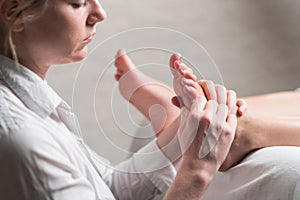 Professional female masseur giving reflexology massage to woman foot