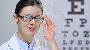 Professional female optician looking at camera against eye chart background