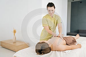 Professional female pediatric masseuse making therapeutic massage on tummy to five year old boy in clinic