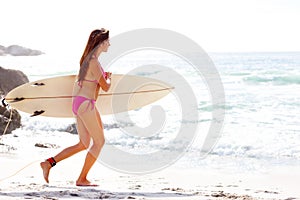 Professional female surfer going for surfing. Portrait of a pretty young female running with a surfboard towards sea.