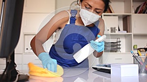 Professional female worker of office cleaning service wearing protective face mask and rubber gloves wiping desk with