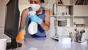 Professional female worker of office cleaning service wearing protective face mask and rubber gloves wiping desk with