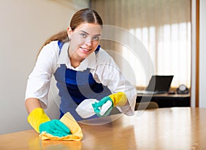 Professional female worker of office cleaning service wiping furniture