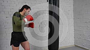 Professional fighter is training in a gym practicing some kicks and punches with punching bag.