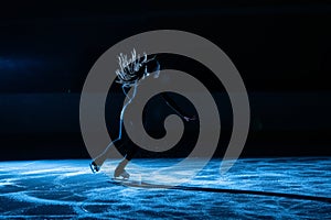 Professional figure skating artist slides and spins on the ice in the arena in the rays of blue light. Young woman