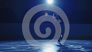 Professional figure skating artist slides and spins on ice arena in rays of blue light. Young woman practicing