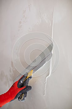 A professional finisher painter levels the walls with putty with a wide spatula