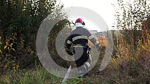 Professional fireman in uniform running for equipment that is in a red truck. Male firefighter jogging through lawn to