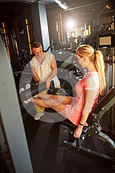 Professional fitness coach assisting lady on a leg extension machine