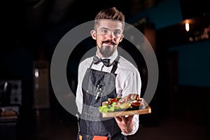 Young garcon offers visitors cooked dish on a black background. photo