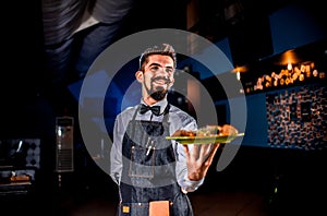 Stylish flunkey carries cooked dish on a black background. photo