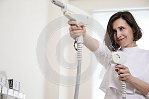 Professional Funny Female Doctor Posing in Doctor`s Smock While Holding Two Intence Pulse Light Apparatus in Laser Rejuvelation
