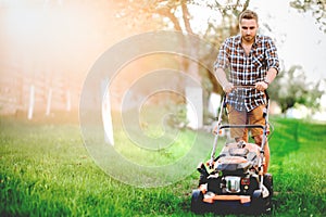 Professional gardener using lawn mower and cutting grass during summer sunset