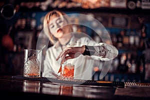 Professional girl bartender decorates colorful concoction while standing near the bar counter in nightclub