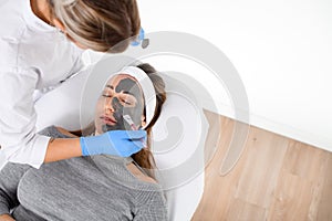 Professional in gloves makes a face mask for a young woman lying on a salon couch