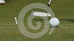 Professional golfer putting ball into the hole. Golf ball by the edge of hole with player in background on a sunny day