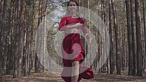 Professional graceful young woman in red dress dancing in the forest landscape. Dancer showing classic ballet poses and