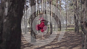 Professional graceful young woman in red dress dancing in the forest landscape. Dancer showing classic ballet poses and