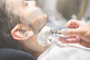 Professional hairdresser applying shaving foam on client skin in barbershop