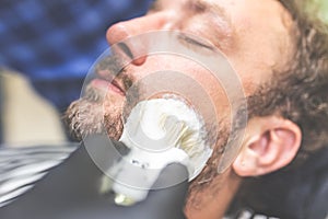 Professional hairdresser applying shaving foam on client skin in barbershop