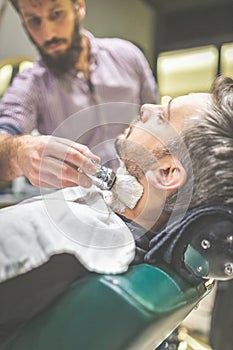 Professional hairdresser applying shaving foam on client skin in barbershop