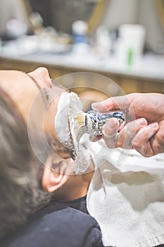 Professional hairdresser applying shaving foam on client skin in barbershop