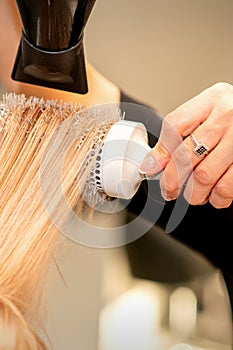 Professional hairdresser dry hair with a hairdryer and round hairbrush in a beauty salon.