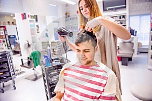 Professional hairdresser drying hair to her handsome client.