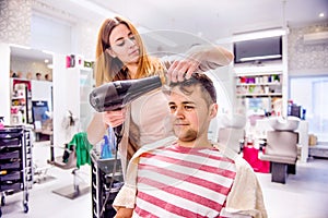 Professional hairdresser drying hair to her handsome client.