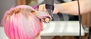 A professional hairdresser is drying long red hair with a hair dryer and round brush, close up.