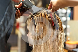 Professional hairdresser dyeing hair of her client in salon. Haircutter dry hair with hairdrier. Selective focus.
