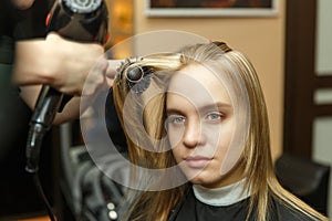 Professional hairdresser dyeing hair of her client in salon. Haircutter dry hair with hairdrier. Selective focus.