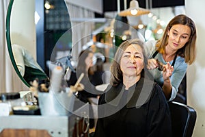 Professional hairdresser examining hair of elderly female client