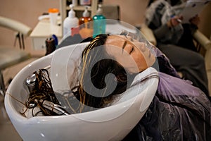 Professional hairdresser, stylist coloring hair of asian woman client  with dark hair at salon