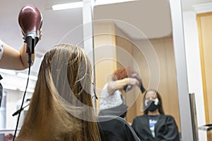 Professional hairdresser,stylist making hairstyle ,drying and blowing hair with a hairdryer in beauty salon,reflected in a mirror.