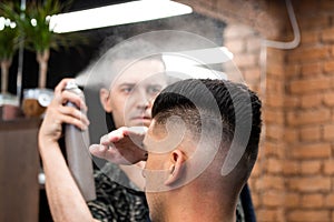 Professional Hairdresser using hair spray on client hair at barber shop, Cool barber splashes from the spray bottle at the hair of