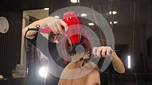 Professional hairdresser using a round brush and hair dryer styling her client's long blonde hair.